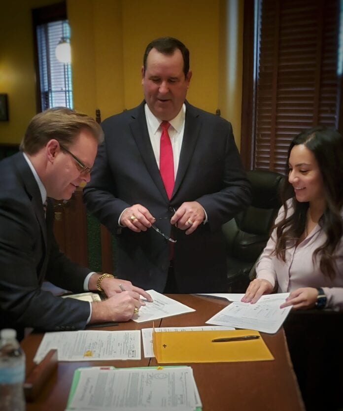 Two men with a woman signing document