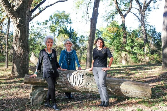 three ladies standing by a log