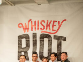 five people standing in front of whiskey Riot sign