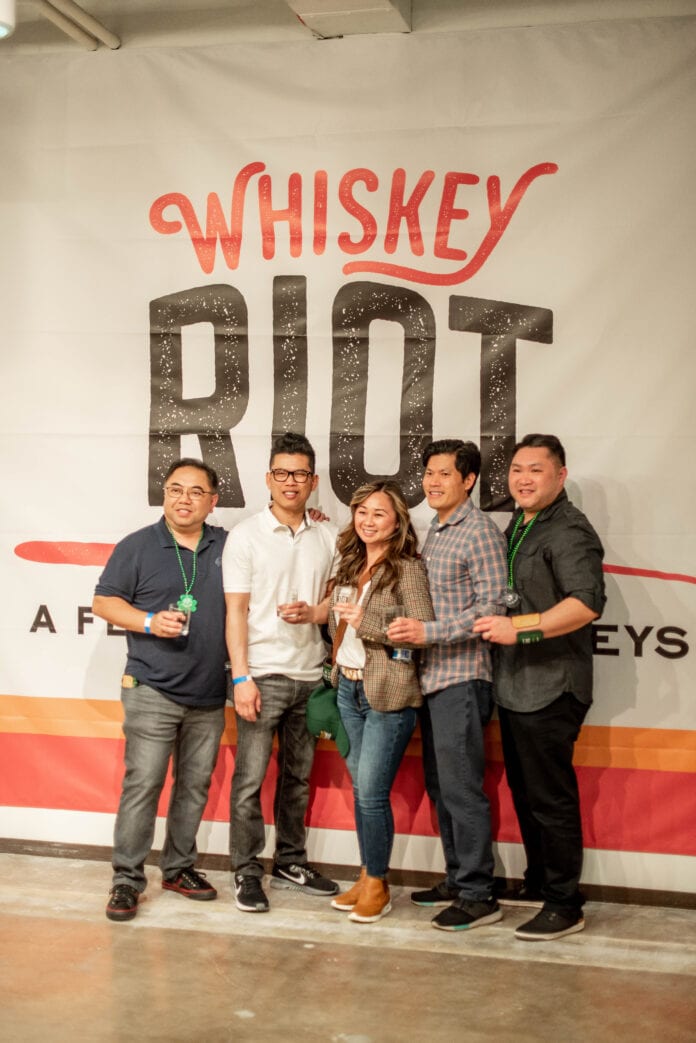 five people standing in front of whiskey Riot sign