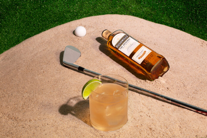 cocktail glass next to golf club in sand bunker