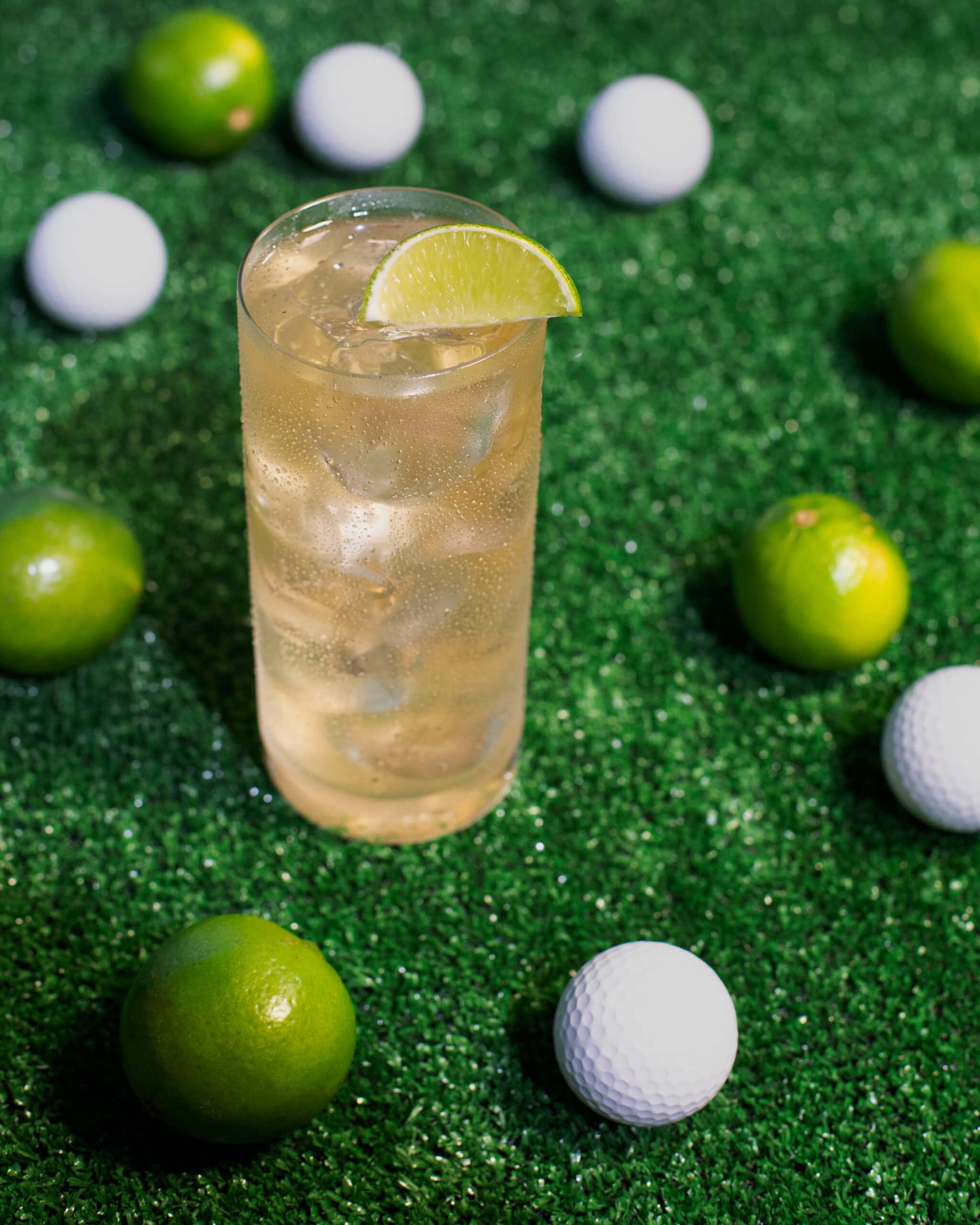 golf members bounce cocktail in highball glass surrounded by limes and golf balls