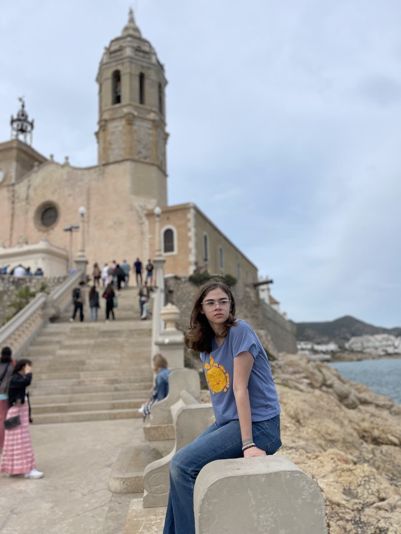 Girl sitting by beach in Sitges with church in background