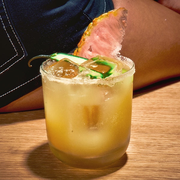cocktail glass with yellow beverage and jalapeno garnish