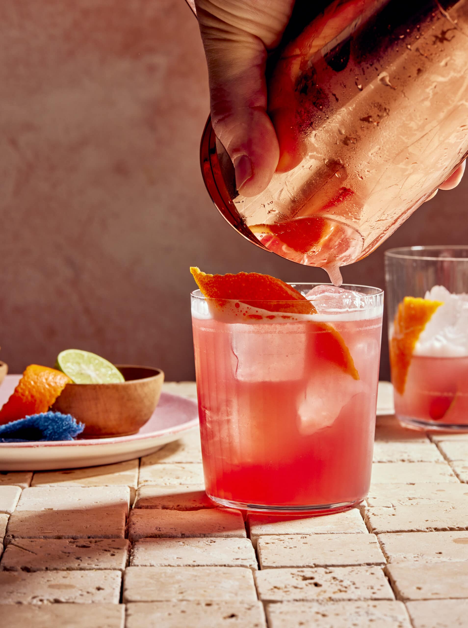 copper cocktail shaker pouring pink drink into rocks glass