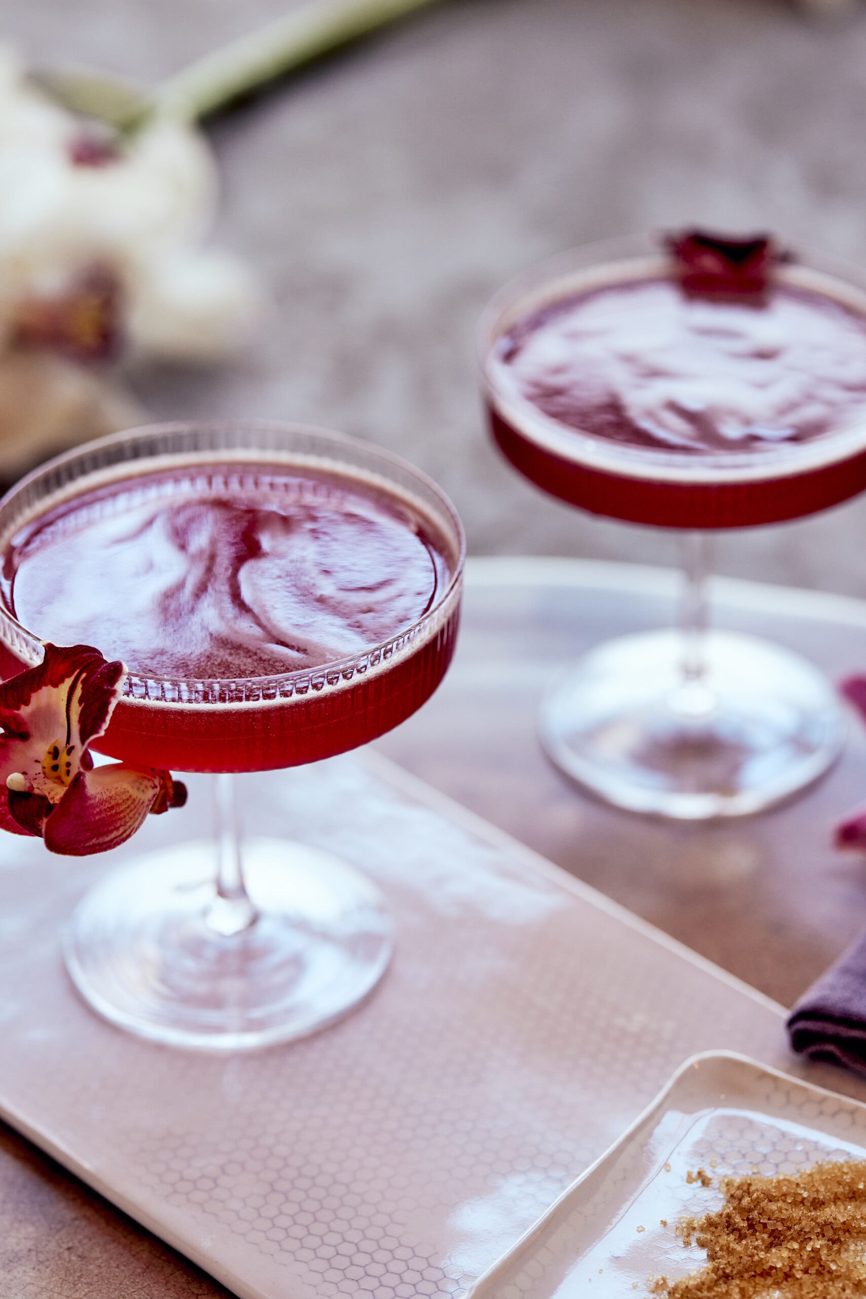 red cocktail in coupe glass with flower garnish