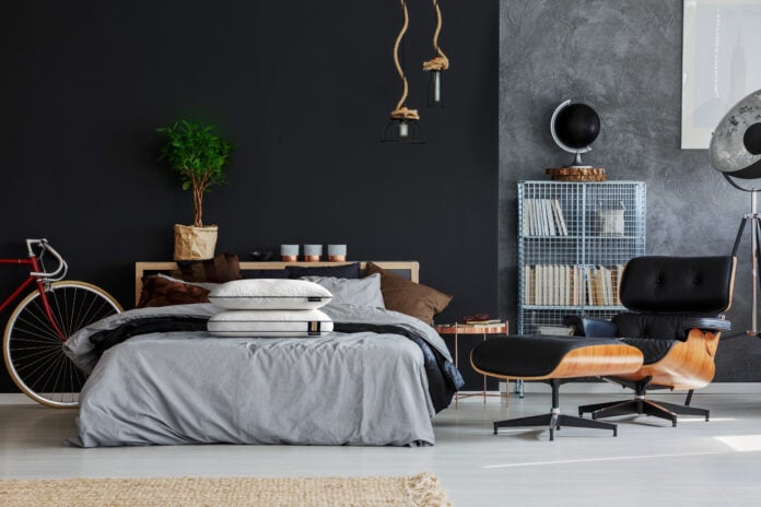 Beige braided pillow on king-size bed with grey coverlet in manly room with black chaise lounge